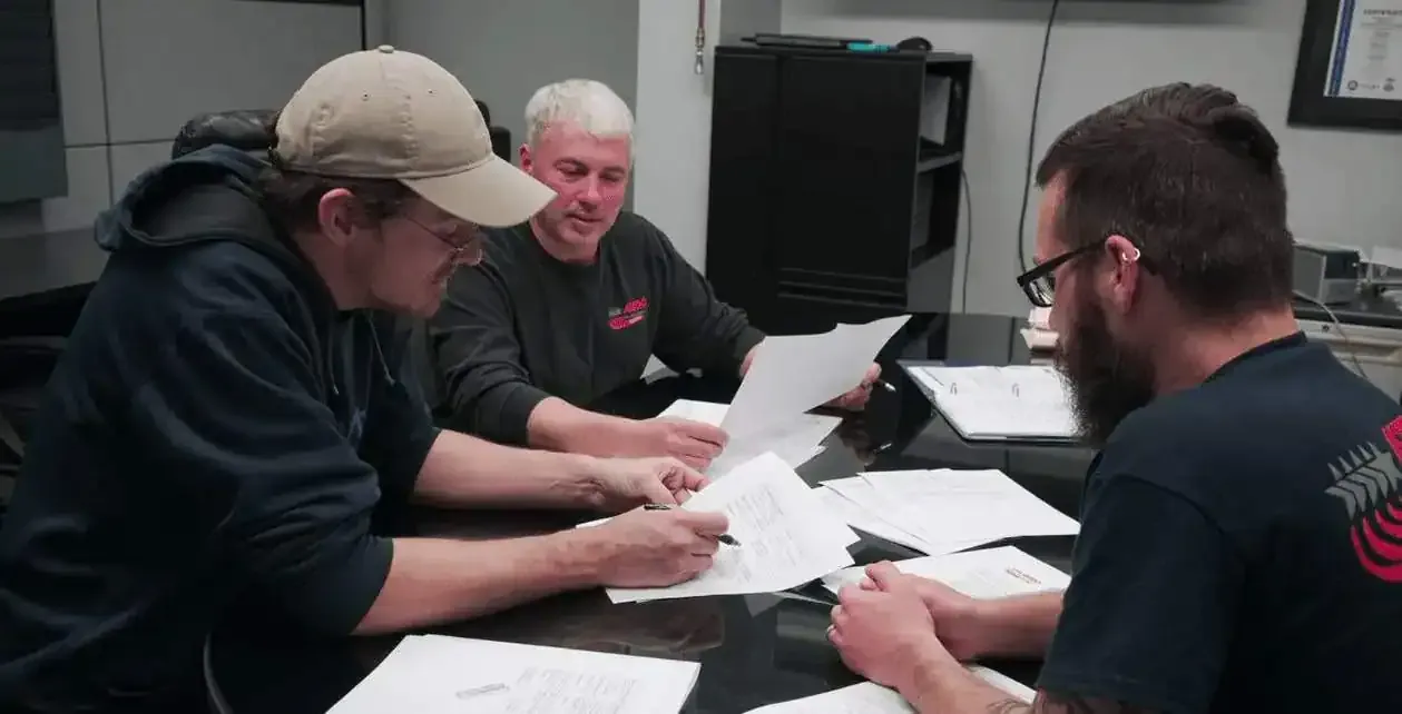 Three Astro team members reviewing part drawings at a table