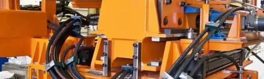 An orange custom machine frame with hydraulic hoses and cable carriers, built by Astro